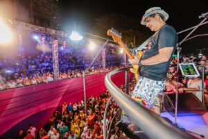 Foto do cantor Durval Lelys em cima do trio elétrico cantando e tocando guitarra para os foliões do bloco Me Abraça